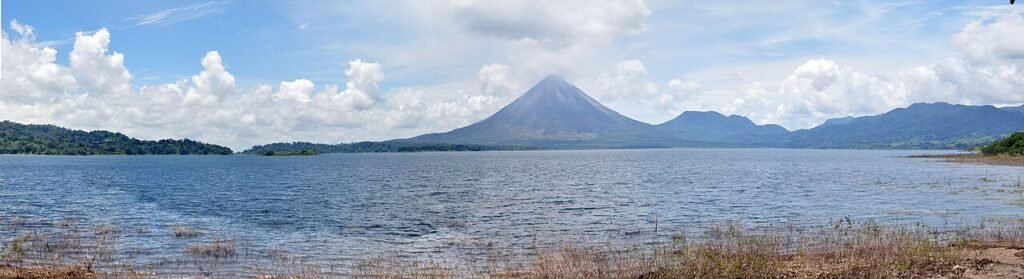 Arenal Volcano across Lake Arenal, with forested shores and tropical clouds in Costa Rica.